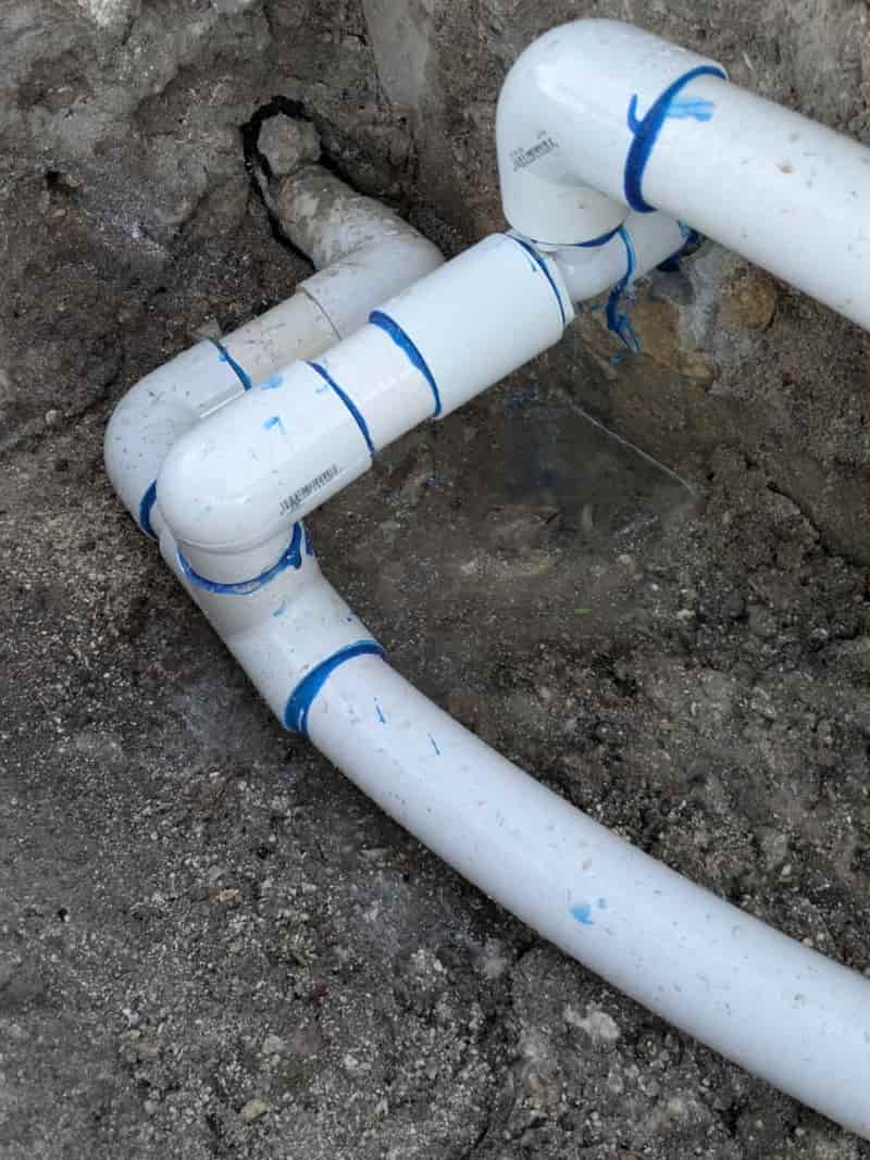 White PVC plumbing pipes and fittings in a dug-out trench