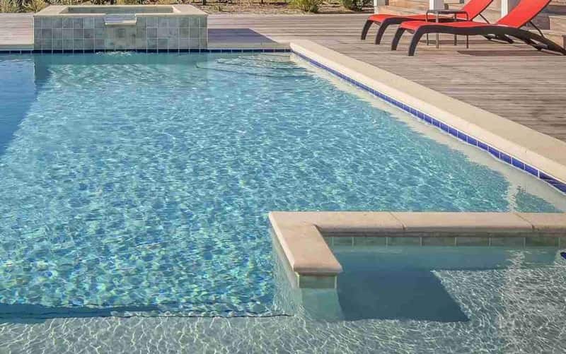 Commercial Pool Leak Detection: a rectangular pool with a raised spa, two stone benches and red lounge chairs on a wooden deck