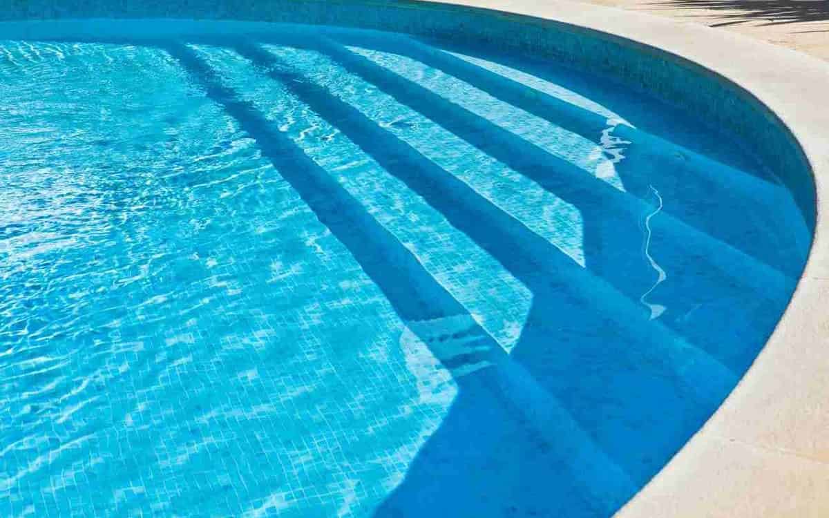 Clear blue pool water over tiled steps beside a pale stone edge that curves around the pool